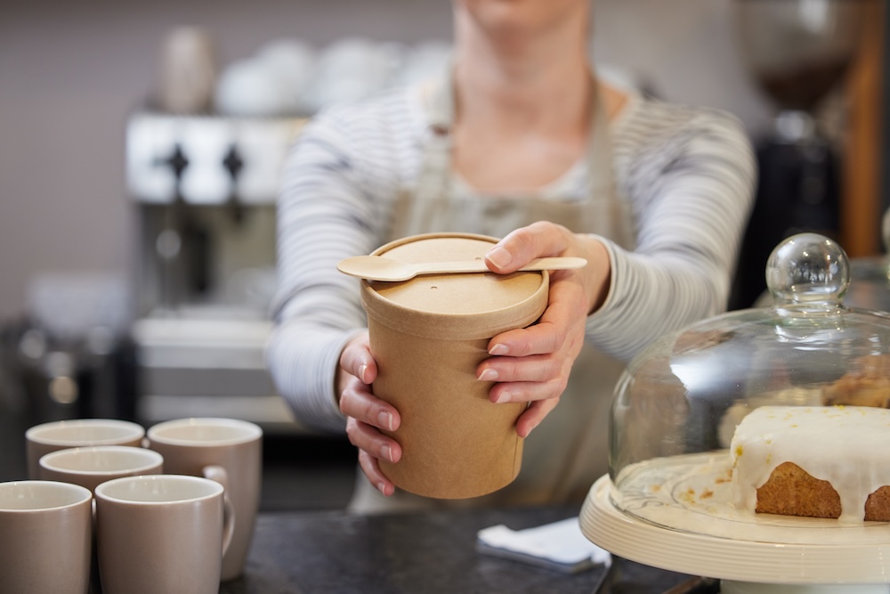 Cafe style packaging; cardboard based lunch food container held by a cafe worker